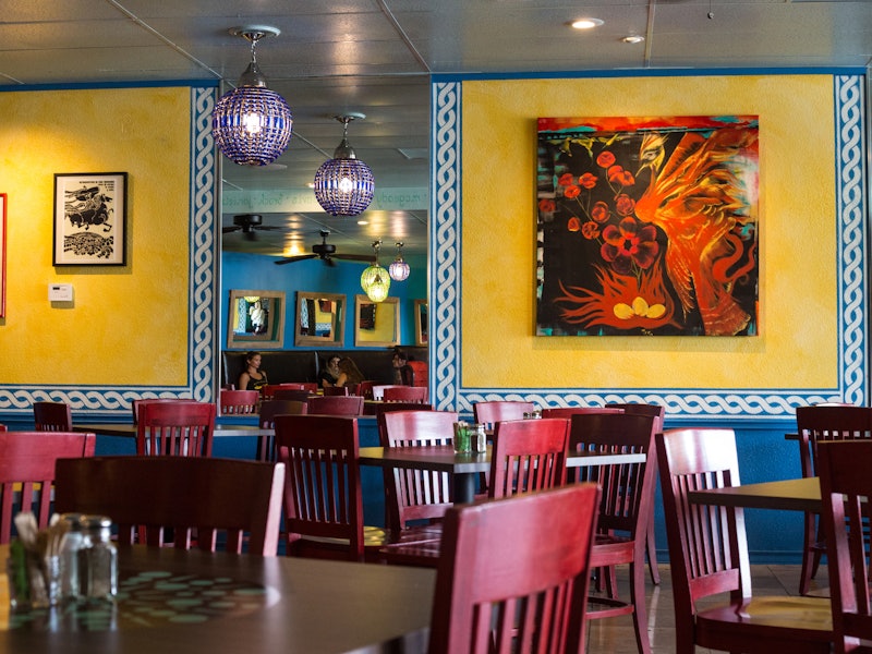 yellow walls with bright artwork behind tables with red chairs at a restaurant 