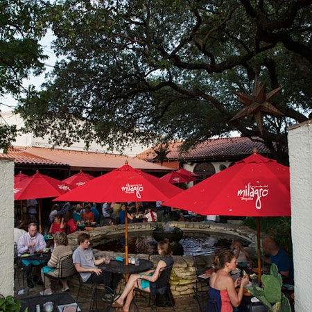Red umbrellas above black tables filled with people surround a stone pool on the patio at Matt's El Rancho